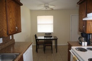 A kitchen with wooden cabinets, a white stove, a dining table with two chairs, and a ceiling fan. - Spacious 2BR/1BA Stay Minutes from Fort Sill (Lawton)