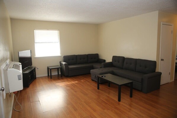 A living room with a sectional sofa, a coffee table, a television, and a window. - Spacious 2BR/1BA Stay Minutes from Fort Sill (Lawton)