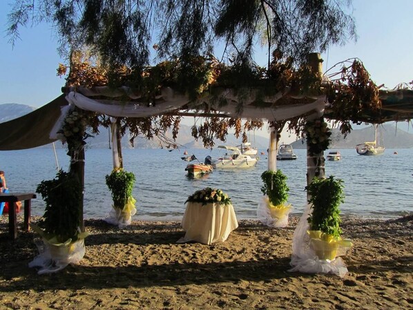 A beach wedding setup with a canopy, potted plants, and a table.