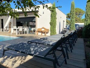 A poolside area with lounge chairs, a wooden bench, and a building with a white exterior.