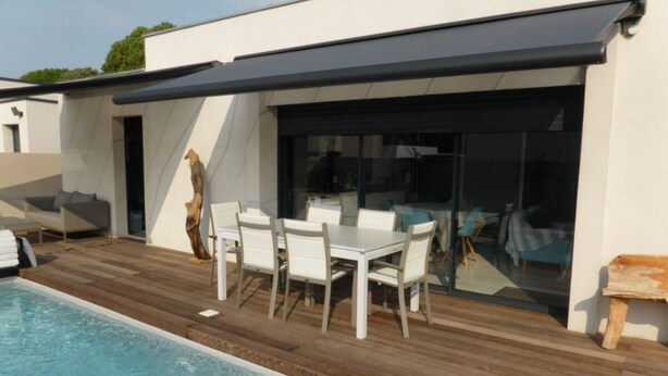 A modern outdoor pool area with a wooden deck, a white table with chairs, and a glass enclosure. - Cala Rossa: MT **** charm + Quality / Price – Private heated pool-Air conditioning- WIFI (Lecci)