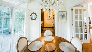 Un espace repas avec une table en bois, des chaises blanches, un lustre et une vue dégagée grâce à de grandes fenêtres.