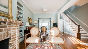 Un vaste salon agrémenté d’une cheminée en briques, de deux fauteuils élégants, d’une table basse et d’un escalier menant à l’étage supérieur.