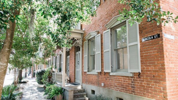 Une rangée de maisons de ville en briques avec des volets blancs, une enseigne indiquant « Lincoln St. », et un trottoir bordé de verdure.