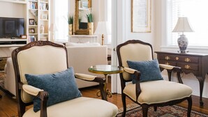 Un salon comprenant deux fauteuils rembourrés, une table basse en verre, un canapé blanc et une table d’appoint en bois avec une lampe.