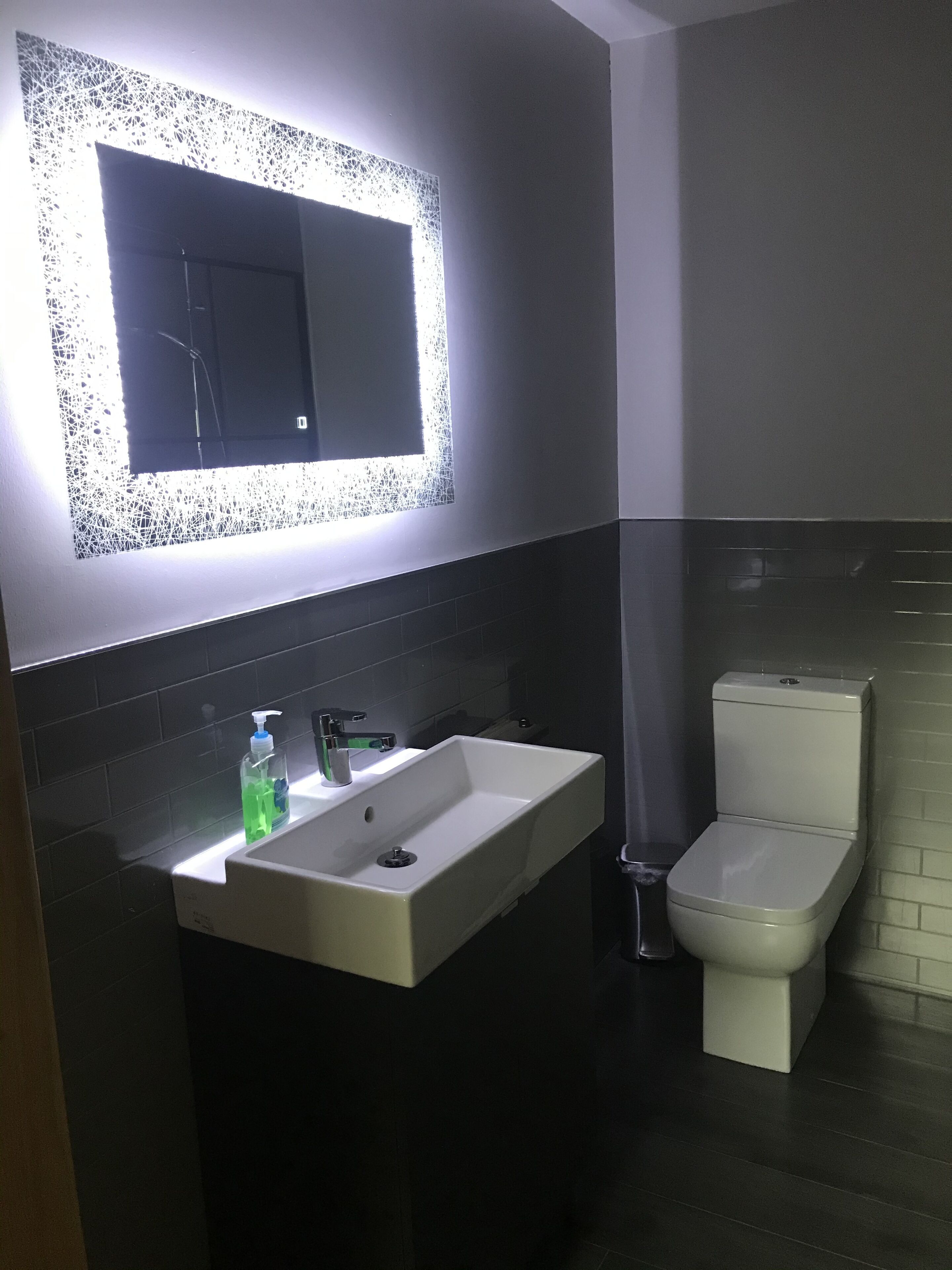 Une salle de bain moderne avec un lavabo rectangulaire, des toilettes et un miroir mural doté d’un cadre décoratif.