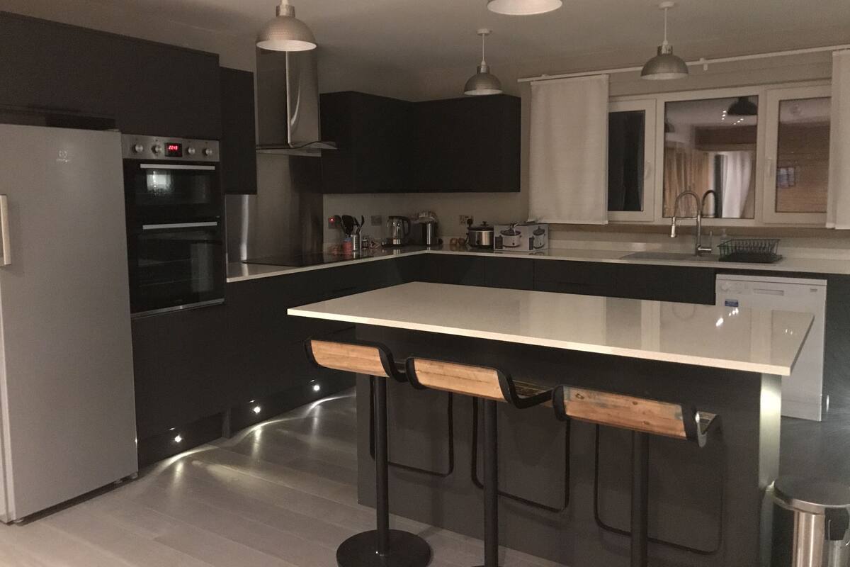 A modern kitchen with a central island, bar stools, a built-in oven, and pendant lighting.