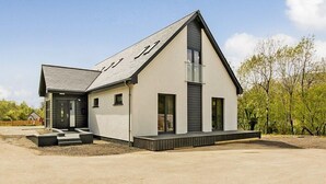 Une maison moderne à deux étages, dotée d’un toit en pente, de grandes fenêtres et d’un petit porche à l’avant.