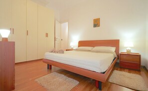 Une chambre à coucher comprenant un lit, une armoire en bois, deux tables de chevet avec des lampes et une porte.