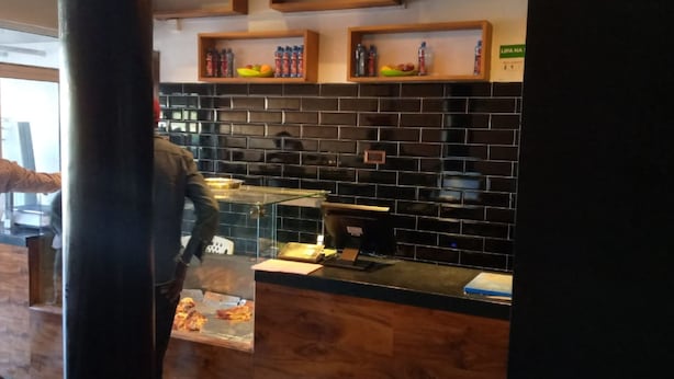 Angolo cottura con schienale nero in piastrelle, mensole in legno con bottiglie d'acqua e un bancone con macchina da caffè.