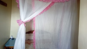 Una stanza con un letto coperto da una tenda bianca con balze rosa. Accanto al letto c'è un tavolino con un rotolo di carta e una scatola.