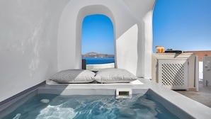 A small, private hot tub with two patterned pillows, a view of the sea, and a clear blue sky. - Utopia Villas - Amaya Selection Of Villas (Santorini)