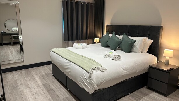 A modern hotel room with a large bed, dark headboard, and two bedside tables with lamps. - 6Adelphi (Preston)