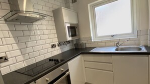 A modern kitchen with white cabinetry, a black countertop, a stainless steel range hood, a microwave, and a window above the sink. - 6Adelphi (Preston)