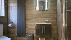 A modern bathroom with a wooden floor, a toilet, a sink with a cabinet, a mirror, and a shower area. - 6Adelphi (Preston)