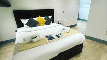 A neatly made bed with a black headboard, white bedding, and a few pillows in different colors. There is a tray with toiletries and a remote control on the bed.
