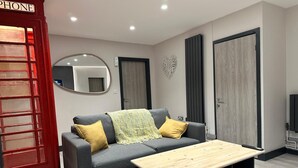 A modern living room with a grey sofa, yellow cushions, a wooden coffee table, a red telephone booth, and a mirror on the wall. - 6Adelphi (Preston)