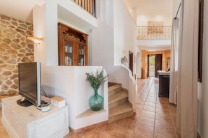 A spacious living area with a stone wall, a wooden bookcase, a flat-screen TV, and a green vase on a white console.