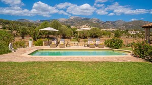 Une piscine entourée de chaises longues et de parasols, bordée d’une pelouse bien entretenue et offrant une vue sur un paysage montagneux.