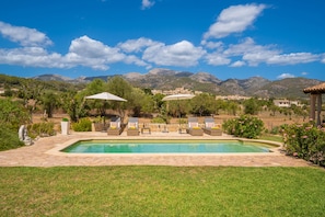 Une piscine entourée de chaises longues et de parasols, bordée d’une pelouse bien entretenue et offrant une vue sur un paysage montagneux.