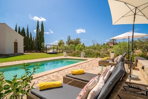 A poolside area with lounge chairs, a pergola, and a view of a house and trees.