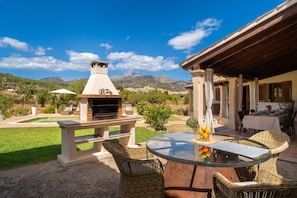 An outdoor patio with a brick barbecue, wicker furniture, and a view of the mountains.