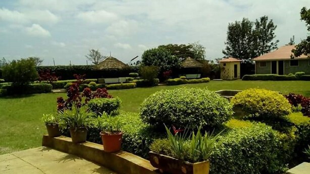 A well-maintained garden with various plants and shrubs, a paved pathway, and a building with a red roof in the background. - Ukombozi Retreat & Conference Centre - Hostel (Thika)