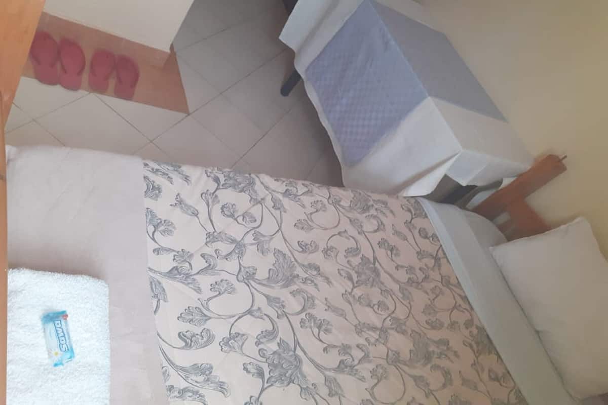 Une pièce avec un lit, une table et une chaise. Une paire de chaussons est posée sur le sol.
