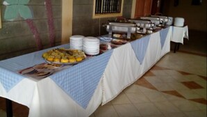A buffet table with various food items and stacked plates, set in a room with tiled flooring and a door in the background. - Ukombozi Retreat & Conference Centre - Hostel (Thika)