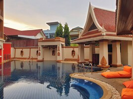 A swimming pool with a tiled floor, surrounded by a building with traditional architectural elements and orange seating.
