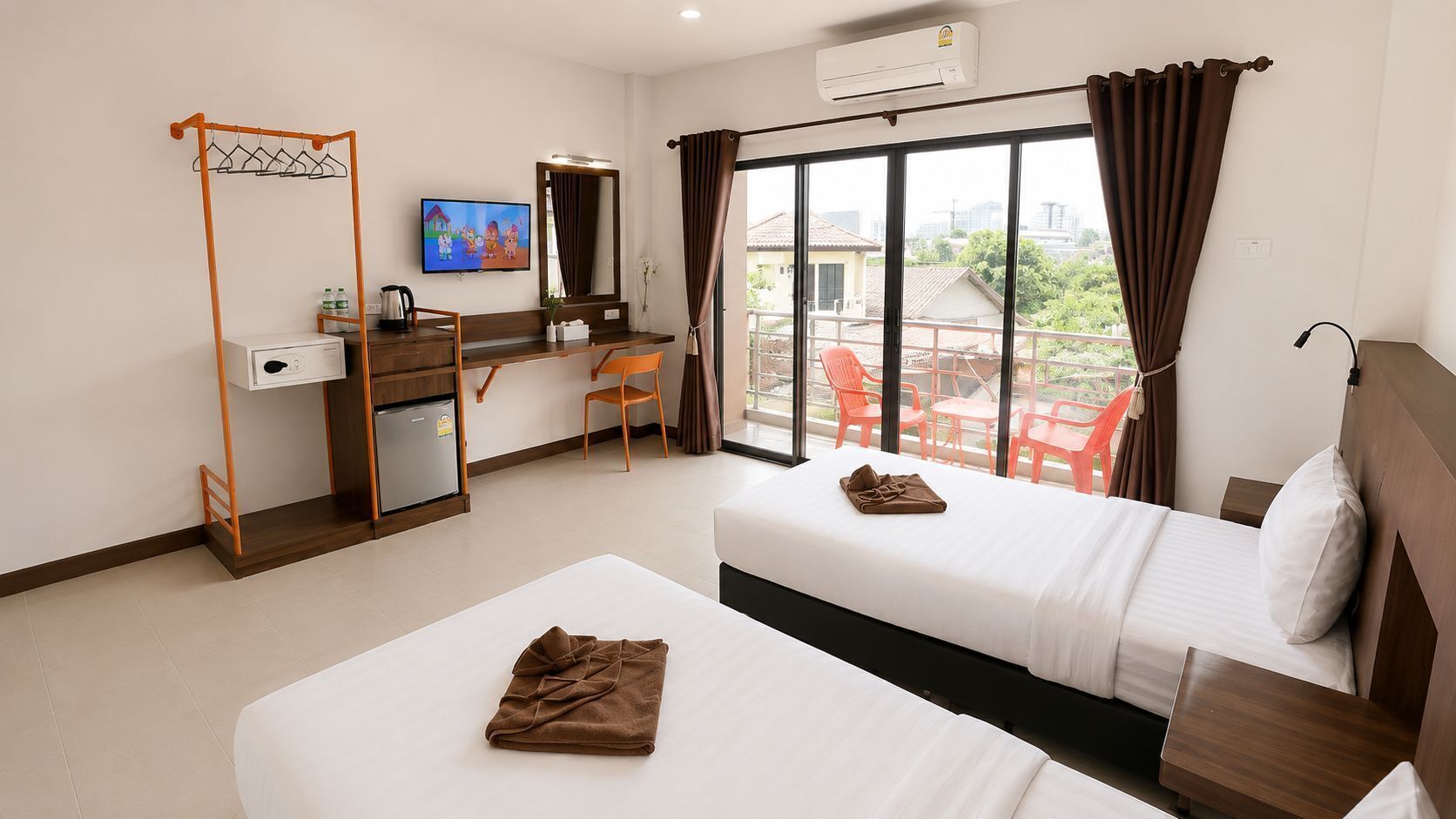 A hotel room with two beds, a desk, a TV, and a balcony with chairs.