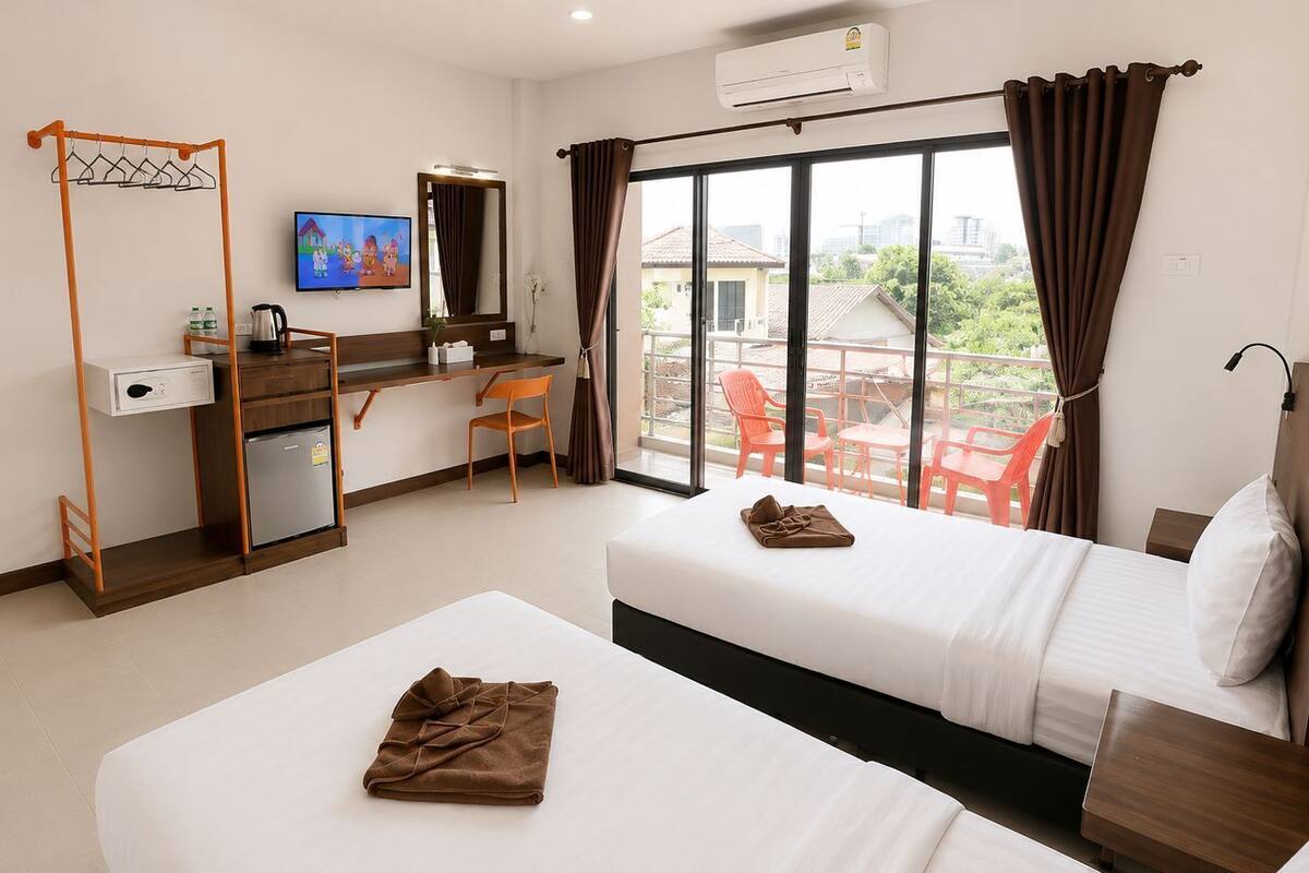 A hotel room with two beds, a desk, a TV, and a balcony with chairs.