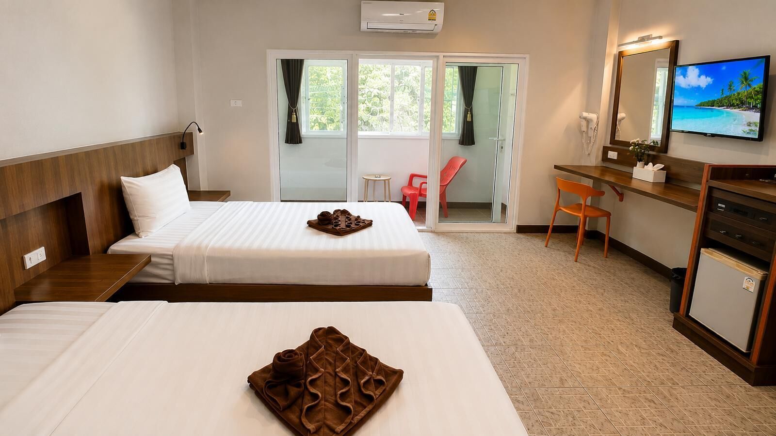 A hotel room with two beds, a desk with a chair, a television, and a sliding glass door to the outside.