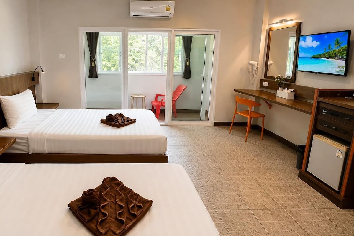 A hotel room with two beds, a desk with a chair, a television, and a sliding glass door to the outside.