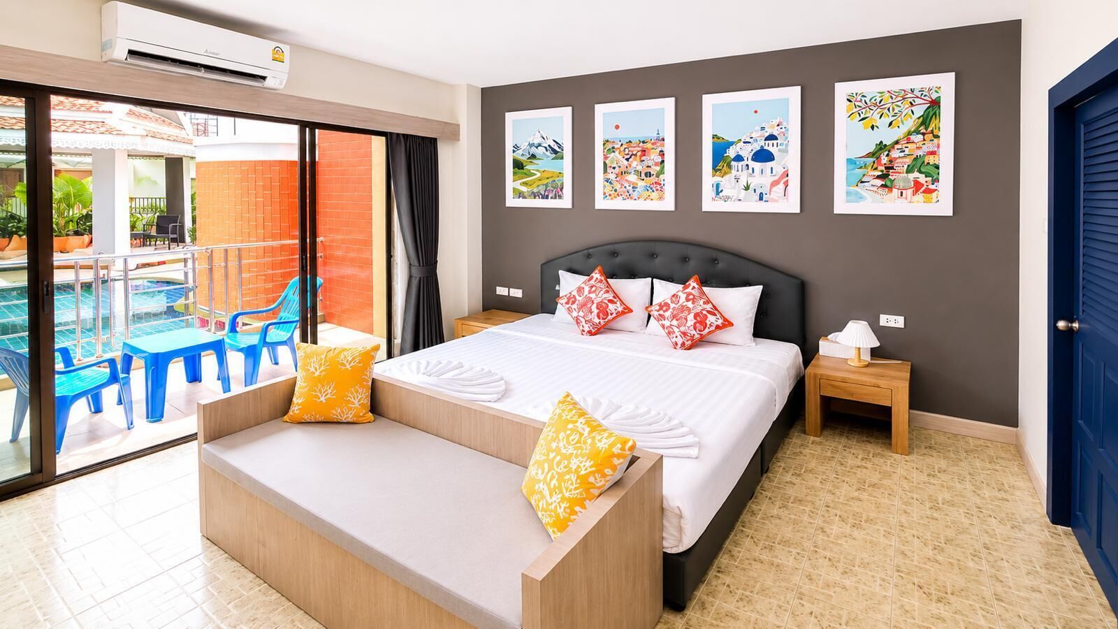 A hotel room with a bed, a bench, a nightstand, and a view of a pool area.