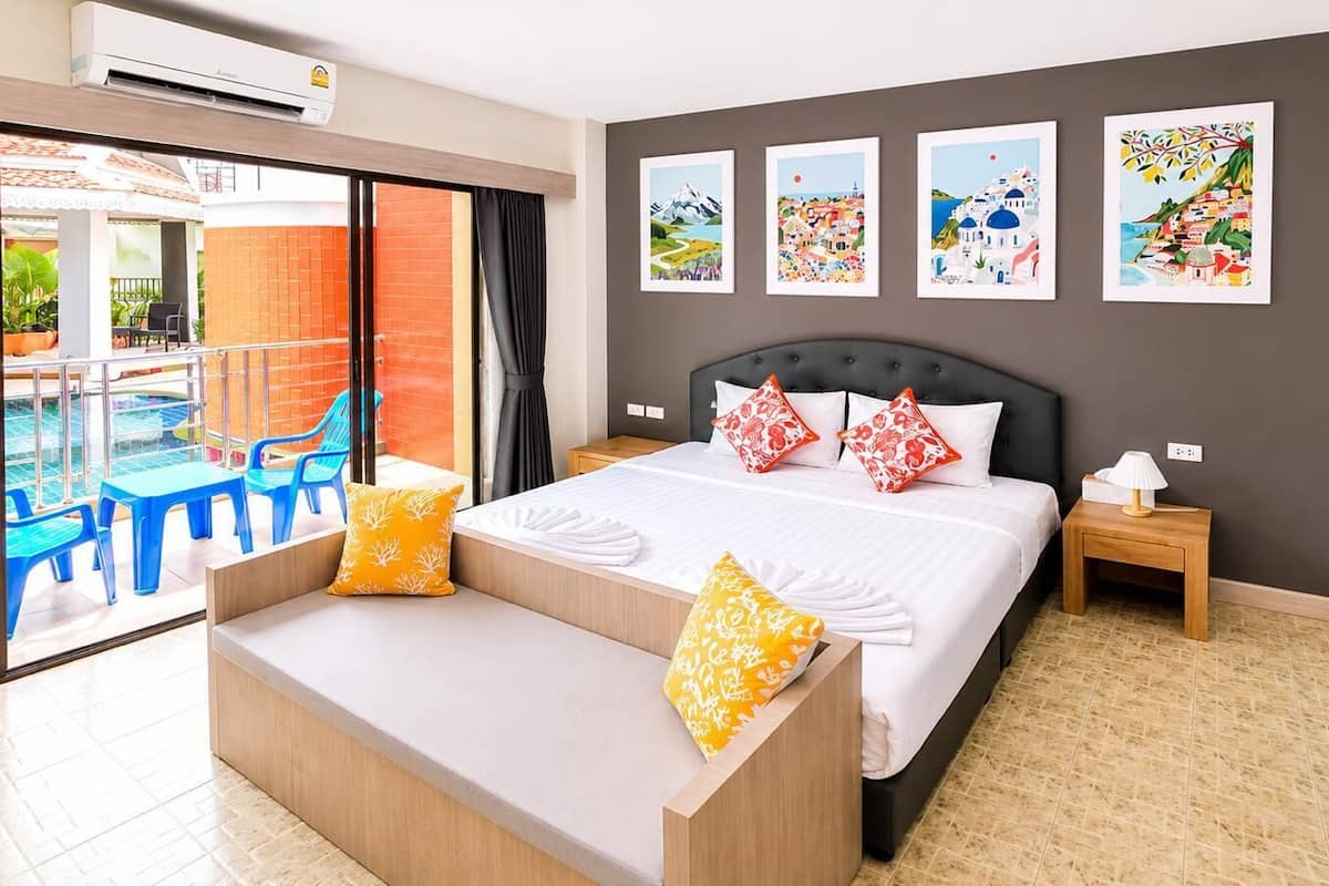 A hotel room with a bed, a bench, a nightstand, and a view of a pool area.