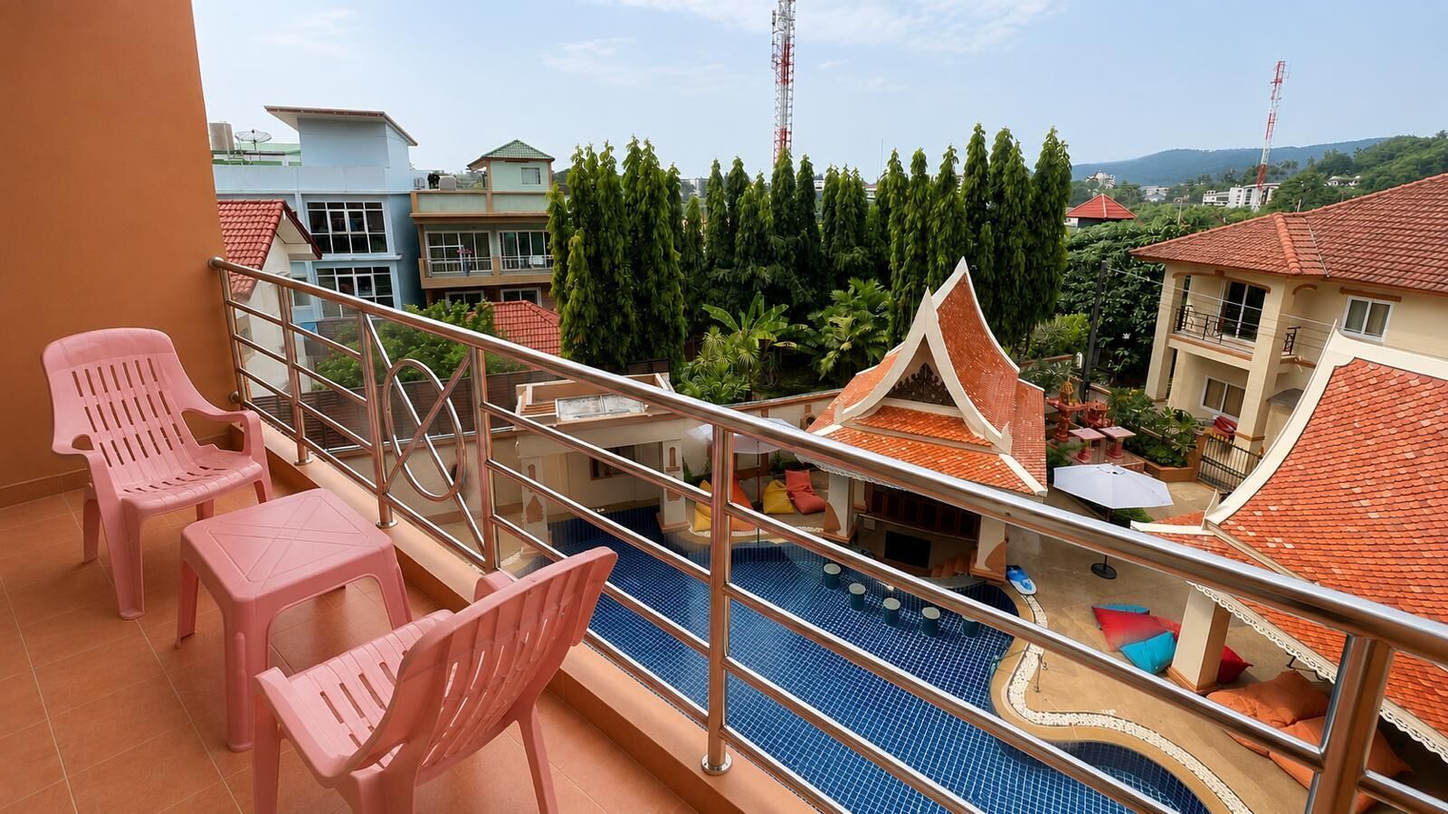 Un balcone con sedie di plastica rosa, una piscina e vista su edifici e alberi.