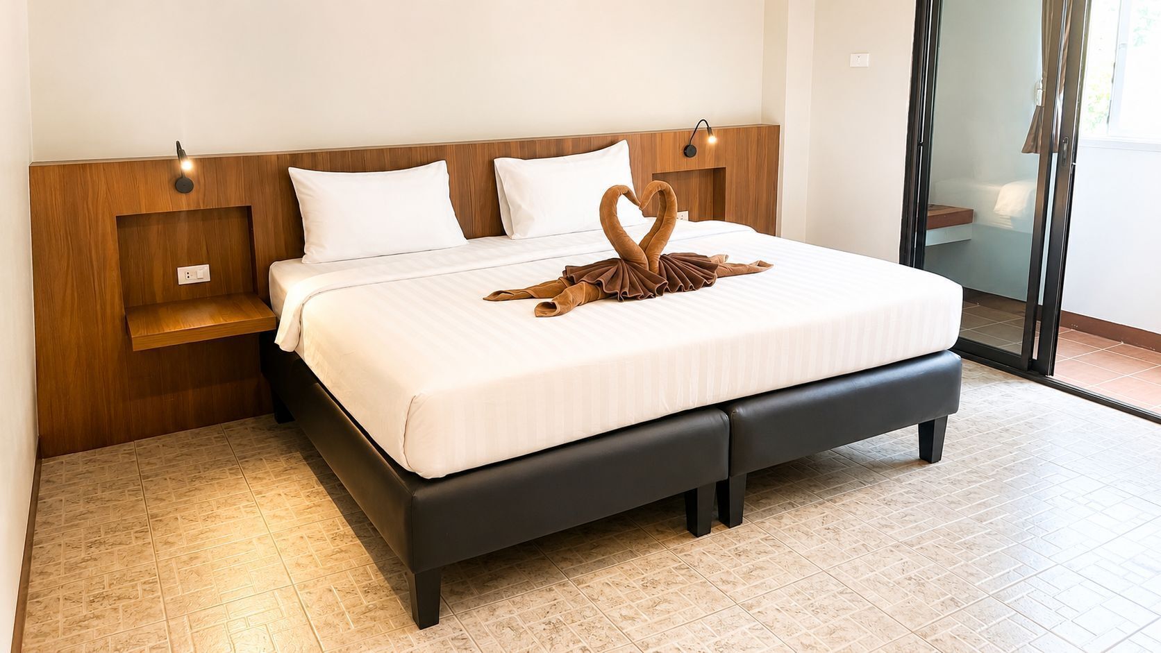 A neatly made bed with a swan-shaped towel, a wooden headboard, and a nightstand with a lamp.