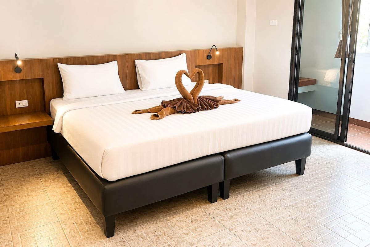 A neatly made bed with a swan-shaped towel, a wooden headboard, and a nightstand with a lamp.