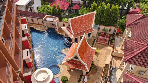 A rooftop swimming pool with a red-tiled roof, surrounded by a building with balconies and a palm tree. - My Friend's House (Karon)