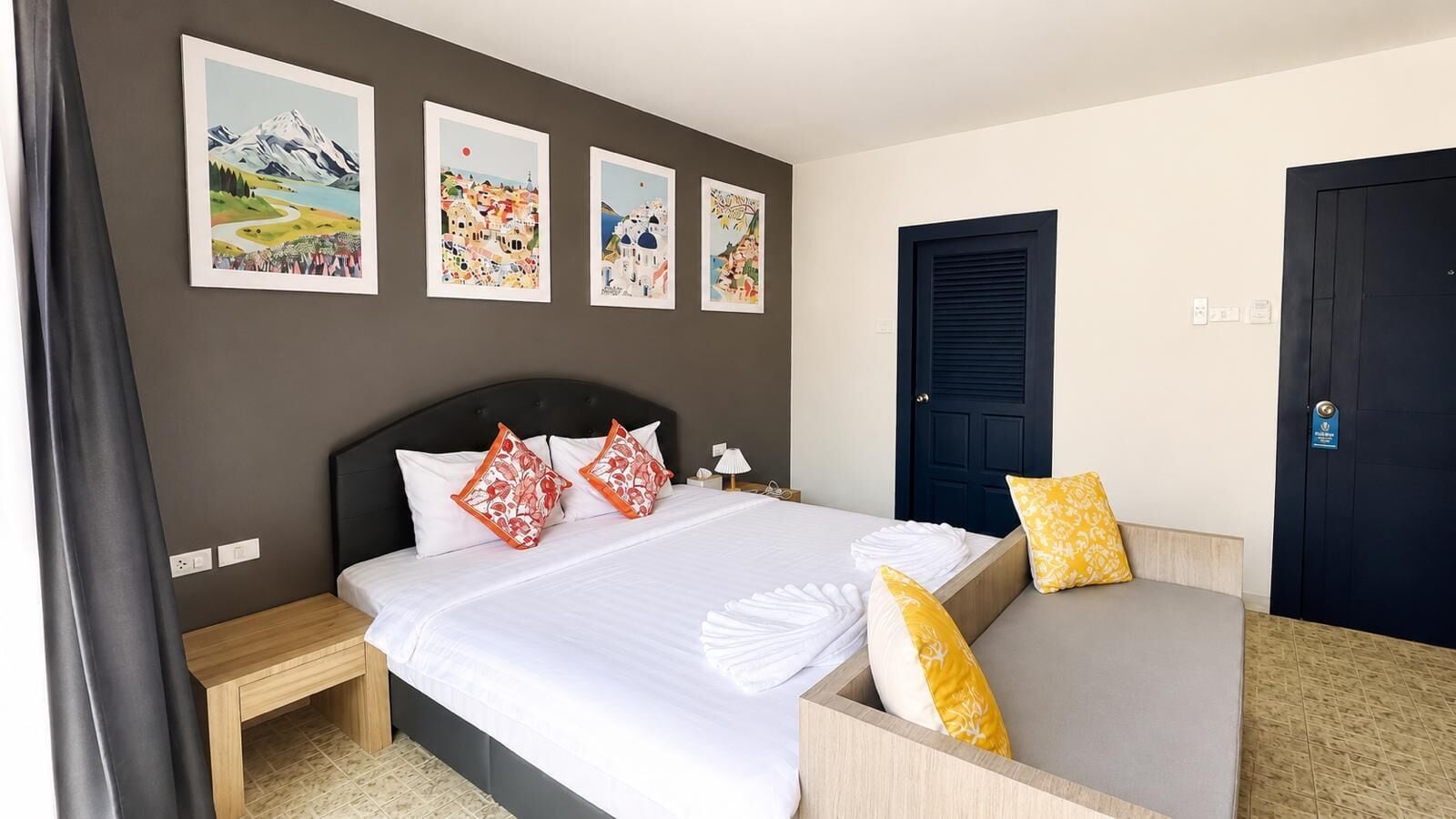 A hotel room with a bed, bedside tables, a sofa, and artwork on the walls.