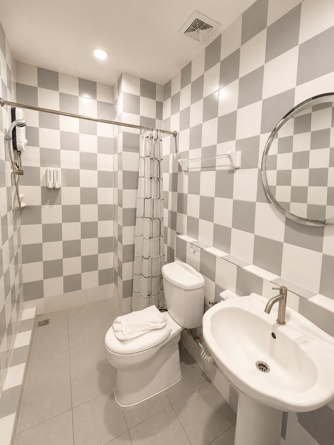 Un bagno moderno con una parete rivestita di piastrelle a scacchi, un water, un lavandino e una tenda da doccia.