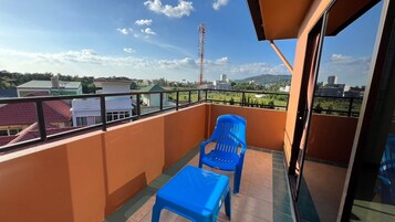 A balcony with a blue plastic chair and table, a clear view of the cityscape, and a tall communication tower in the distance.