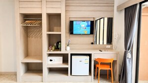 A compact hotel room with a wooden wardrobe, a small desk with a refrigerator, a television, and an orange chair. - My Friend's House (Karon)