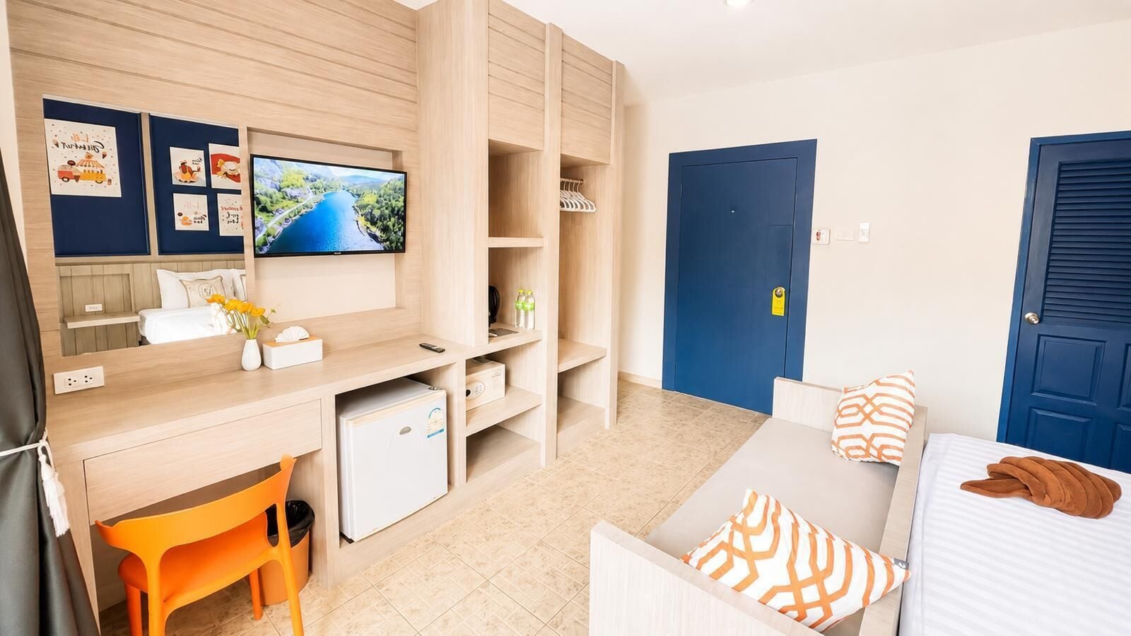 A modern hotel room with a desk, bed, TV, and storage units.