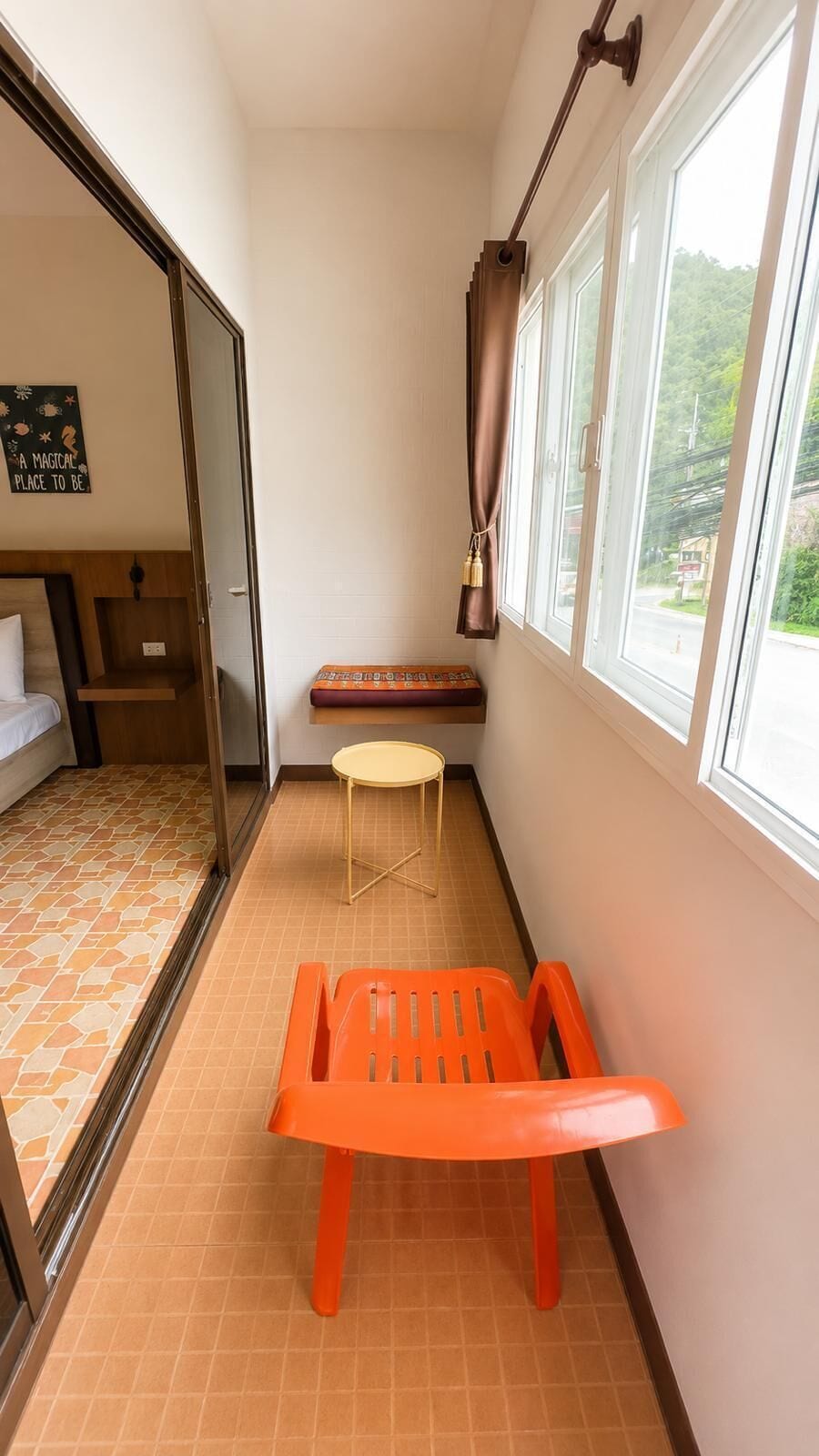 A small room with a bed, a table, a bench, and a window with a view of greenery.