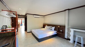 A hotel room with a bed, a desk, and a chair. There is a window and an air conditioning unit on the wall. - My Friend's House (Karon)