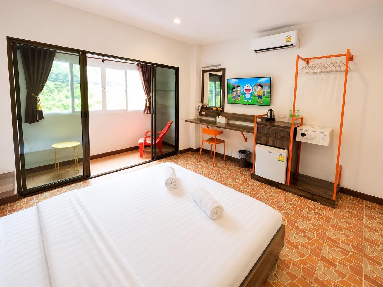 A hotel room with a bed, a desk, a television, and a sliding glass door leading to a balcony.
