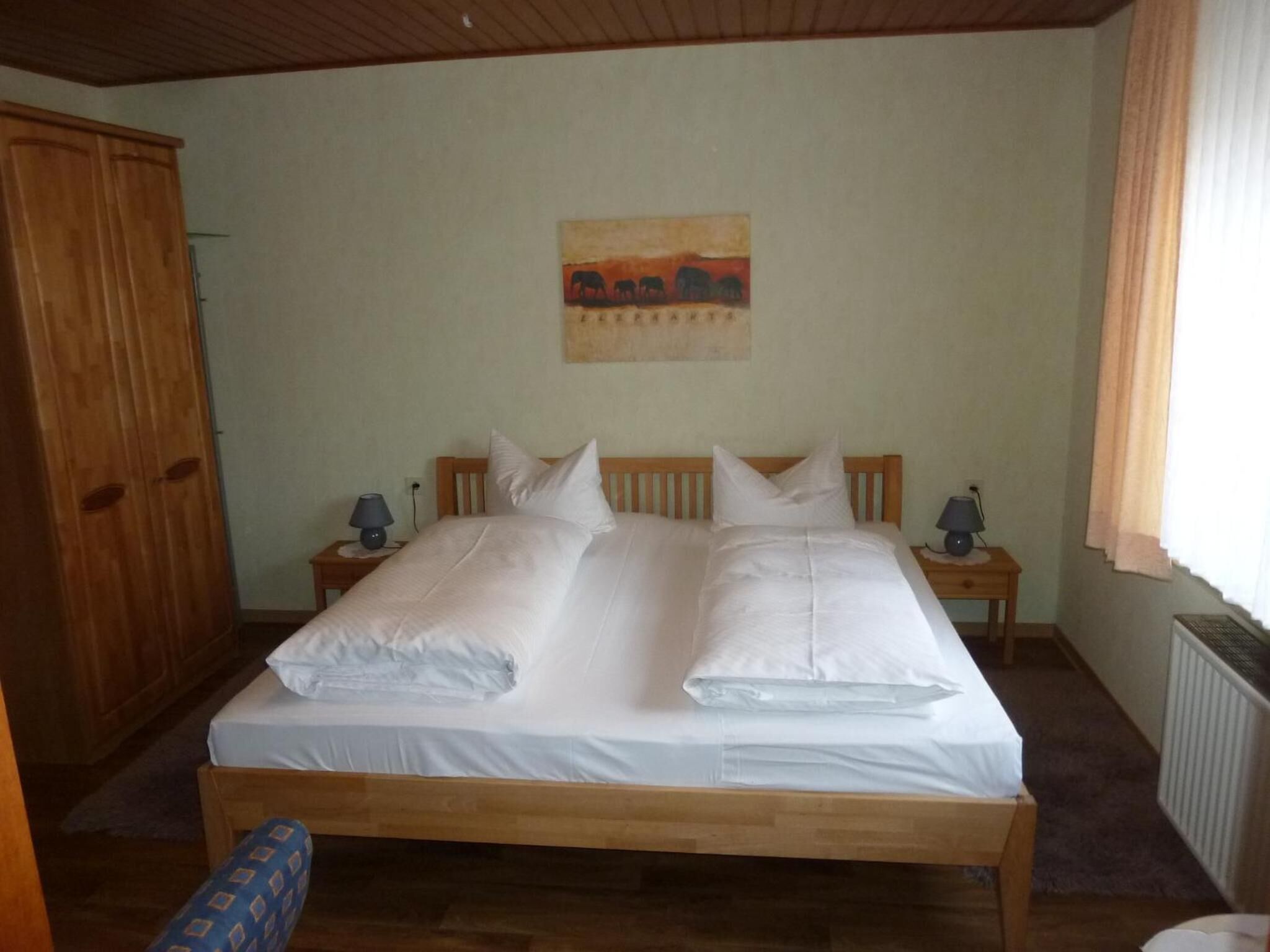 A bedroom with a wooden bed, two bedside tables with lamps, a wooden wardrobe, and a painting on the wall.