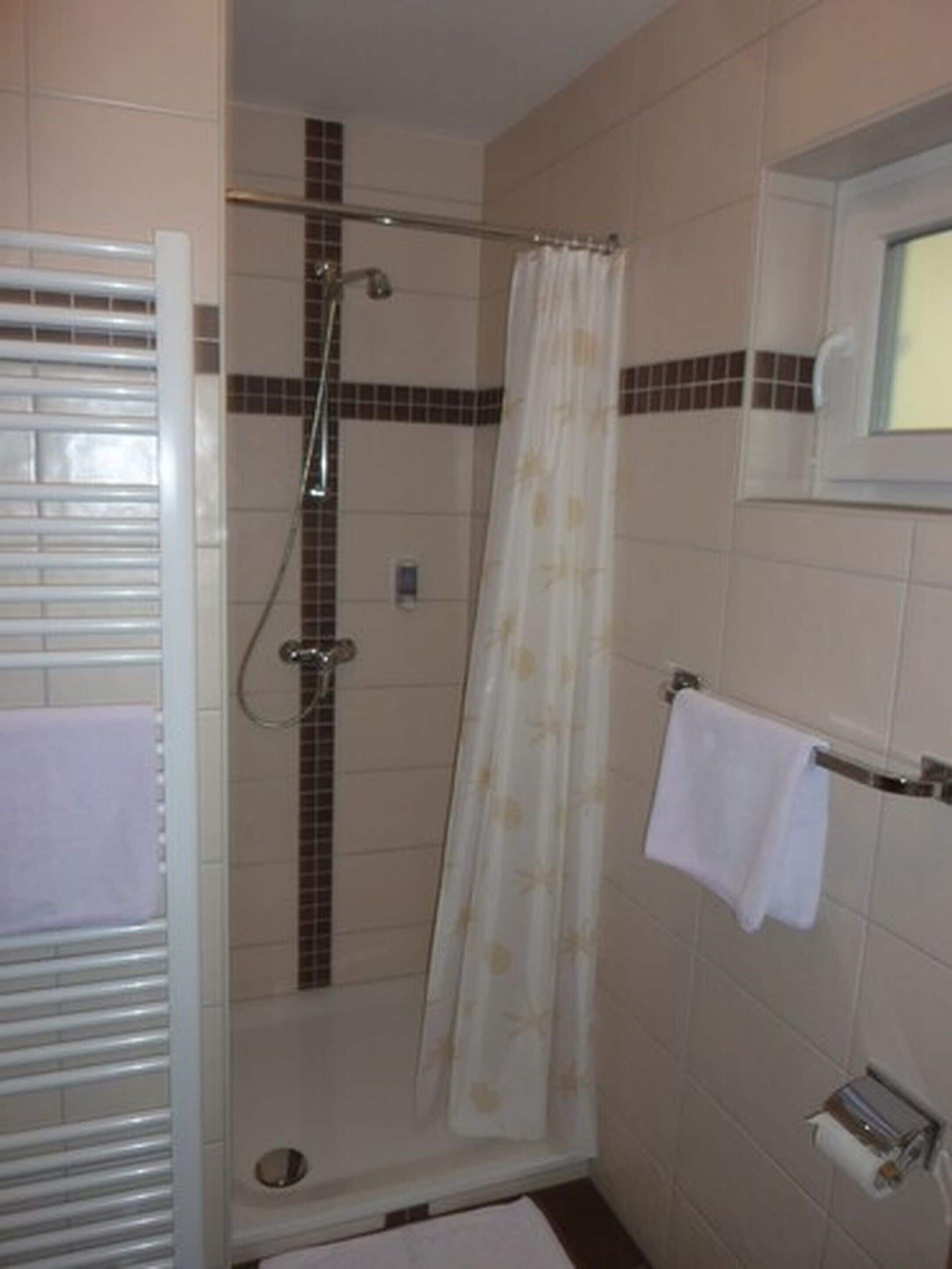 A shower area with a glass door, a showerhead, a curtain, and a towel rack with a towel.